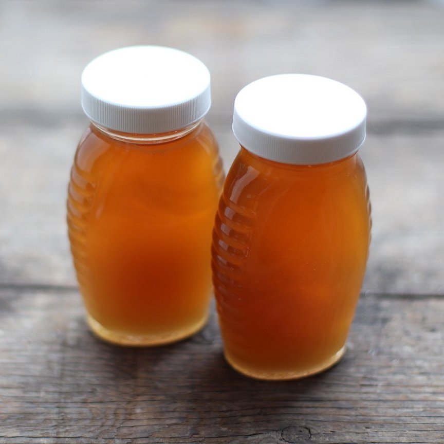 honey_jars Two jars of golden honey with white lids sitting on a rustic wooden surface.